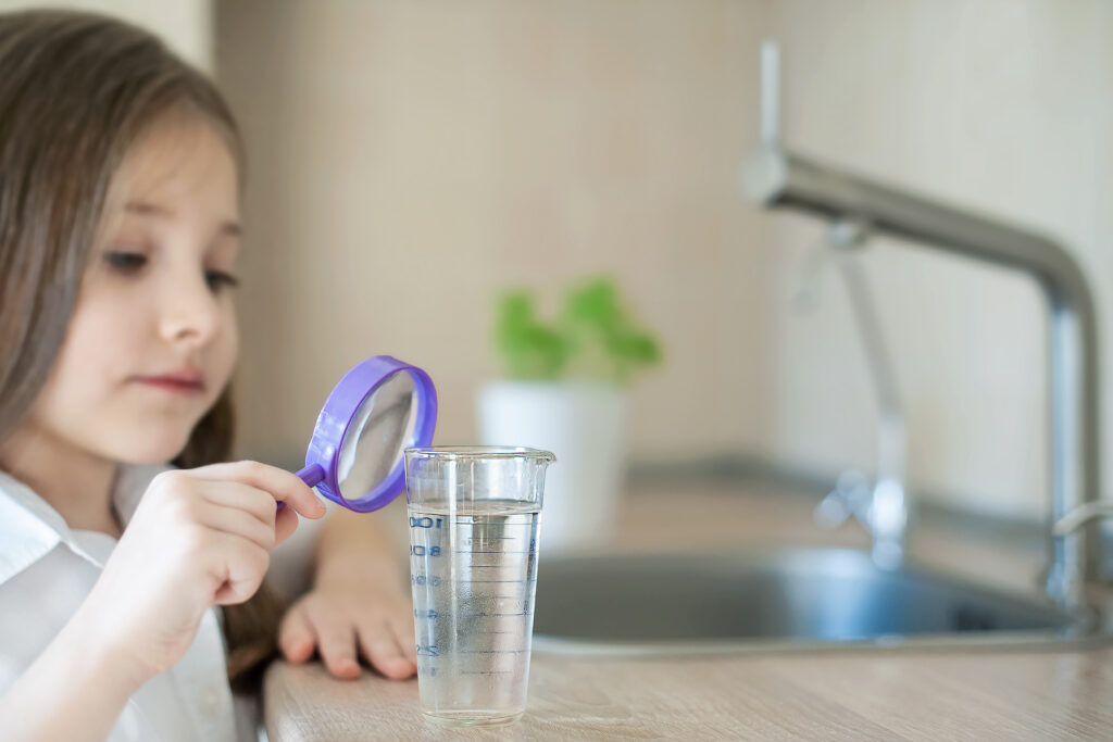 Eine Hand hält eine Lupe und blickt auf Wasser zum Wassertest: Symbolisiert das Konzept der Analytik für Wassertests.